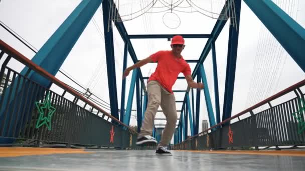 熟練したヒップスターは スタイリッシュな布を着用しながら 低角度のカメラで橋で足を踏みます プロのストレスダンサー練習ブレイクダンス 現代のライフスタイル アウトドアスポーツ 2024 スプライトリー — ストック動画