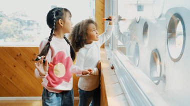 Afrikalı yaratıcı öğrencinin resim dersinde cam tahtada güzel bir resim çizmesi. Asyalı arkadaş birlikte çizim yaparken, kız işaret çizimi yapıyor. Yaratıcılık online eğitim konsepti. Etkinlik.