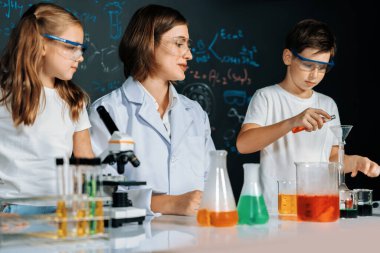 Laboratuvarda çalışan öğretmen, güvenlik gözlüğü takıyor, STEM sınıfında kimya bilimi üzerine deney yapıyor. Öğrenci komedisi tüpte sıvı deneyi yapar. Etkinlik.