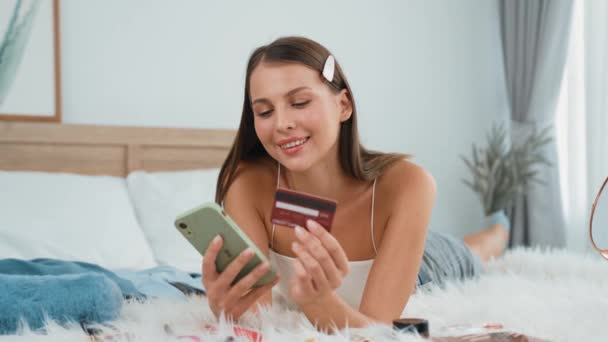 オンライン決済アプリとスマートフォンのデジタルウォレットを使用してベッドに横たわる若い女性は クレジットカードで支払う モバイルインターネットを介して商業ショッピングとモダンな購入 アディット — ストック動画
