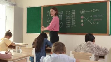 Profesyonel mutlu öğretmen sınıfta oturan çeşitli mutlu öğrencilerden not defteri toplar. Kafkas hocası sınıfta dolaşırken çocukların ödevlerini topluyor. Eğitim konsepti. Pedagoji.
