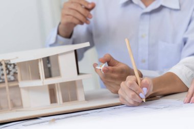 Professional male engineer hand measure house model by using ruler while beautiful cooperative coworker working together by writing on blueprint. Creative design and teamwork. Closeup. Immaculate. clipart