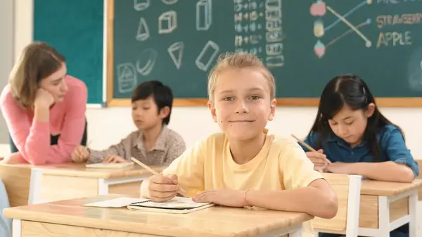 白种人聪明的孩子在课堂上做功课时对着相机微笑 而多文化的快乐学生在小学课堂上做测试或写便条 教育概念 教育学 — 图库照片