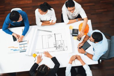 Mimari proje üzerinde birlikte çalışan, inşaat planını gözden geçiren ve toplantı masasında plan oluşturan çeşitli inşaat mühendisi ve müşteri gruplarından oluşan üst düzey bir pankart. Tedbirli