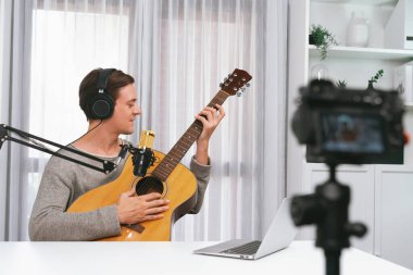 Akıllı şarkıcının sunucu kanalı kamerayla kaydediliyor, gitar çalıyor, sosyal medya kanalından yayın yapıyor, kulaklık takıyor ve beyaz modern stüdyoda video kaydediyor. Bireysel.