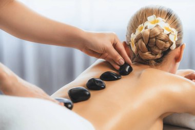 Lüks tatil köyündeki kaplıcalarda sıcak taş masajı. Gün ışığı sükunet ortamında, mutlu kadın müşteri bazalt taş masajından zevk alıyor. Rahatlatıcı bir sıcaklıkla vücudun üzerinde süzülüyor. Sessiz.