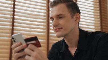 Masada oturan genç adam kredi kartıyla ödeme yapmak için akıllı telefondaki dijital cüzdanı ve uygulamayı kullanıyor. Mobil internet üzerinden alışveriş ve modern alımlar. Düzenle