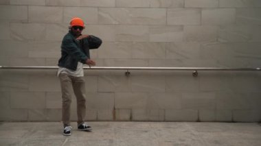 Asyalı akıllı hipster, kulaklık ve şık kıyafetler giyip hip hop şarkıları dinlerken gri arka planlı enerjik break dans gösterisi yapıyor. Açık hava sporu 2024. Hip hop hareketi. Yumuşak bir şekilde..