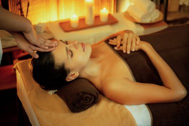 Beyaz kadın stres önleyici kafa masajı yapmaktan ve lüks otel veya otelde sıcak mum ışığında yüz güzelliği eğlencesi yapmaktan zevk alıyor. Sessiz.