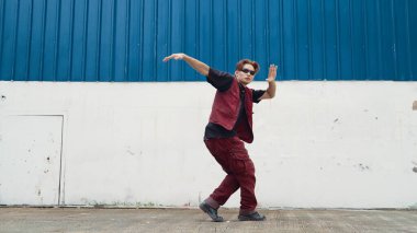 Beyaz arka planda break dans pratiği yapan yakışıklı bir sokak dansçısı. Hip hop tarzı giyinen sporcu, mavi arka planlı bir sokakta müzik eşliğinde ayak sesleri çıkarıyor. Açık hava sporu 2024. ÇalışmaComment.