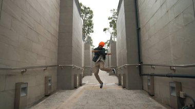 Yakışıklı Asyalı hippi koridorda yürürken dans ediyor. Profesyonel break dansçı kameraya bakarken şık kıyafetler giyiyor. Açık hava sporu 2024. Sokak dansı, break dans. Yumuşak bir şekilde..