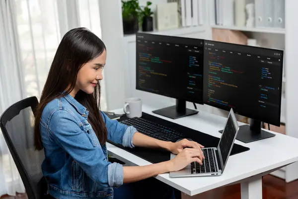 Smiling young Asian in IT developer creating with typing online information on laptop with coding program data of application, wearing jeans shirt. surrounded by safety analysis two screen. Stratagem.