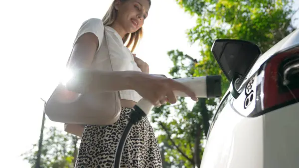 阳光灿烂的年轻女子乘坐电动车在绿色可持续城市室外花园充电 电动汽车内部的绿色城市可持续发展生活方式 — 图库照片