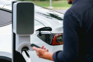 Ulusal Park veya Yaz Ormanı 'ndaki tatil gezisi sırasında EV şarj istasyonundan elektrik aküsü almak için akıllı telefon internet bankacılık uygulaması kullanan bir adam. Yükselt