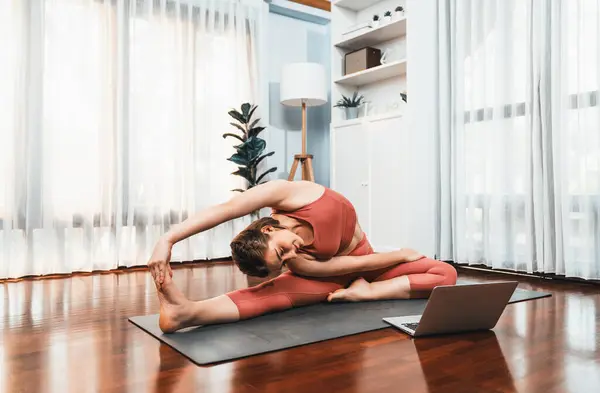 自宅での運動マットの瞑想姿勢でヨガ姿勢をしているスポーツウェアの柔軟でデクスタリティの女性 平和な心と静けさで健康的なヨガオンライントレーニングセッション — ストック写真