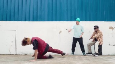 Genç Asyalı dansçı hip hop tarzında dans ediyor ve çok kültürlü arkadaşları duvarın arkasında tezahürat yapıyor. Çekici yakışıklı adam mavi arka planda kollarını uzatıyor. Açık hava sporu 2024 hiphop..