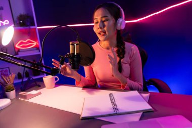 Geceleri podcast 'te olumlu konuşmalar yapan, pembe neon ışıklı modern stüdyoda sunum için dizüstü bilgisayar kullanan, gülümseyen, genç, güzel Asyalı bir etkileyiciydi. Taktik.