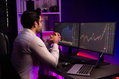 Akıllı tüccar işadamı, karanlık oda gecesinde neon ışıklı ofisteki arama pazarında yüksek kârla ekranda bilgisayar ve bilgisayar üzerinde dinamik borsa yatırımları üzerinde yoğunlaşıyor. Tahmin et..