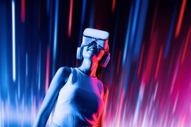 Zeki bir kadın, metaevreni birbirine bağlayan VR kulaklık takan neon ışıklarla çevrili duruyor. Gelecekteki siber uzay topluluğu teknolojisi. Uzaklara bakan zarif bir kadın ve tatmin edici bir şekilde gülümsüyor. Halüsinasyon.