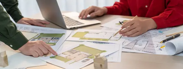 A portrait of skillful architect discussing with his coworker about house construction design during using laptop. Professional engineers choose house plan carefully. Closeup. Delineation.