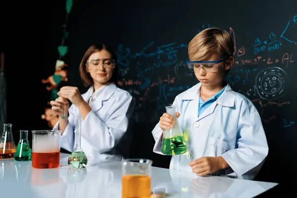 Teacher support schoolboy in laboratory they wear lab coat and glasses stand and experiment about science of chemistry in STEM class. Student tong solid down to yellow liquid in beaker. Erudition.