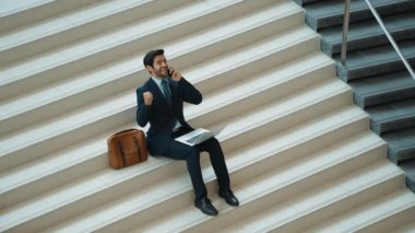 Üst düzey bir iş adamı başarılı projeyi merdivenlerde oturup dizüstü bilgisayar analiz verilerini kullanarak kutluyor. Menajer yeni bir iş buluyor, terfi alıyor ve telefonla arkadaşlarını arıyor. Sevinçli..