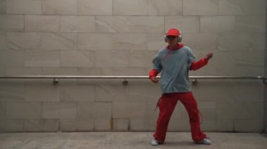 Yakışıklı koreograf gri arka planda sokak dansı yapıyor. Genç çekici erkek dansçı şık kıyafetler giyerken gösteri yapıyor. Hareketli bir adım. Uzayı kopyala Açık hava sporu 2024. Yumuşak bir şekilde..