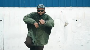 Sokak ortasında mavi duvarlı hippi dansçı ayak basamağı. Asyalı break dansçı kollarını açarken sokak dansı yapıyor. Hip hop koreografı enerjik bir dans sergiliyor. Açık hava sporu 2024 hiphop..