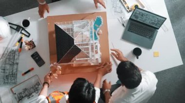 Kalem ölçme evi modelini kullanan yetenekli mimar tasarımcı takımının üst görüntüsü. Bir grup inşaat mühendisi planlama ve tasarım yaparken aynı zamanda dizüstü bilgisayarla masaya işaret ediyorlar. Hizalama.