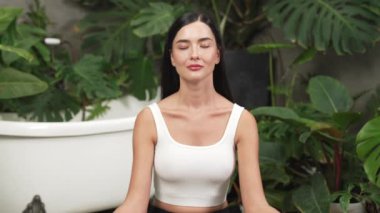 Sabah yoga ve meditasyon yapan genç bir kadın bitki yaprağıyla doğal bahçede yalnızlığın tadını çıkarıyor ve meditasyon yapıyor. Farkındalık aktivitesi ve sağlıklı zihin yaşam tarzı. Blithe