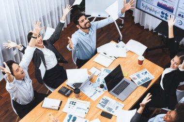 Üst düzey ofis çalışanı toplantı odasında kutlama yapıyor, evrak işlerini havaya fırlatıyor. İş adamlarından gelen heyecan ve özgürlük ifadesi, finansal analiz kağıtlarını kutlama jesti olarak fırlatıyor. Uyum
