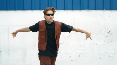Beyaz arka planda break dans pratiği yapan yakışıklı bir sokak dansçısı. Hip hop tarzı giyinen sporcu, mavi arka planlı bir sokakta müzik eşliğinde ayak sesleri çıkarıyor. Açık hava sporu 2024. ÇalışmaComment.