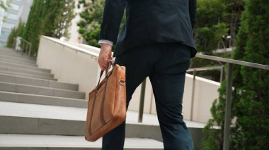 Yeşil şehirde bavulunu tutarken resmi takım elbiseli beyaz bir müdürün merdivenlerden çıkışının arka görüntüsü. Profesyonel bir iş adamı iş yerine giderken aynı zamanda Eko Şehri 'nde merdivenleri çıkıyor. Urbane..