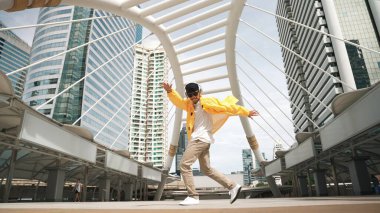Asyalı şık bir adam düşük açılı kamerayla hiphop dansı yapıyor. Break dansçı, şehirde kulaklıktan müzik dinleyip dans ederken merdivenlerden çıkıyor. Açık hava sporu 2024. Yumuşak bir şekilde..