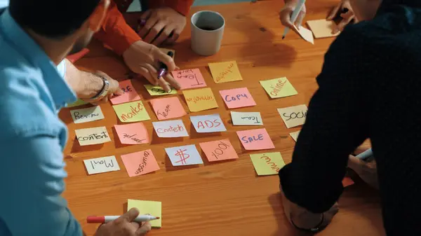 Top down aerial view of creative people hands writing idea on sticky notes at meeting table. Close up of diverse business people hand in casual cloth placed planning strategy on table. Convocation.