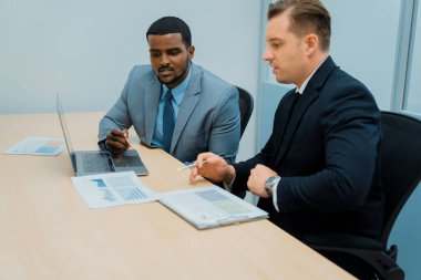 Afrikalı erkek lider stratejiyi açıklarken profesyonel proje yöneticisine çözümünü dizüstü bilgisayar kullanarak belgeye işaret ederek gösteriyor. Yetenekli iş adamlarının beyin fırtınası fikri. İş toplantısı. Süslü.