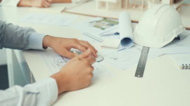 Becerikli mimar mühendis elinin kapanışı, planlı, mimari teçhizatlı, ev modelli ve güvenlik kasklı toplantı masasının planlarını çiziyor. Eline odaklan. Tertemiz..