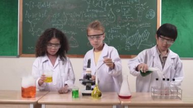 Çocuklar laboratuvarda karatahta başında dururken fen dersinde deney yapıyorlar. Mutlu öğrenci biyokimyasal sıvıyı keşfederken ve incelerken ve karıştırırken. Pedagoji.