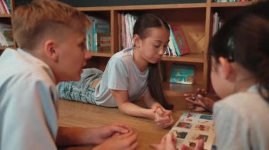 Akıllı kız, çocuk kütüphanede çeşitli arkadaşlarıyla konuşurken resimli kitaba bakıyor. Bir grup çocuk kitabı paylaşırken sevimli bir lise öğrencisi kitaplığın yanında daireler çizerek yatıyor. Öğretim