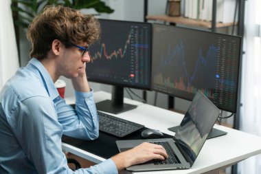 Monitörlerdeki gerçek zamanlı dizüstü bilgisayarda pazar stoğu grafik veri yatırımına odaklanan genç bir tüccar üzerinde çalışıyor. Modern ofiste. Dinamik para bozdurma oranını analiz etme kavramı. Toplayıcı.