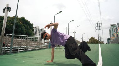 Düşük açılı hipster kamerası kameraya bakarken donuk poz veriyor. Bir grup break dansçı mutlu adam break dans antrenmanı yapıyor. Modern yaşam tarzı. Açık hava sporu 2024. Yumuşak bir şekilde..