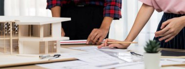 Akıllı mimar mühendis ve iç mimar birlikte çalışıyor ve ev modelini ölçmek için plan ve mimari ekipmanlarla toplantı masasında cetvel kullanıyor. Takım çalışması konsepti. Filizlenen.