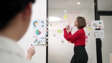 Yetenekli genç ve güzel iş kadını, yaratıcı iş toplantısında yakışıklı yönetici dinlerken zihin haritalama ve istatistiksel grafik kullanarak pazarlama fikrini kendine güvenle sunuyor. Tertemiz..