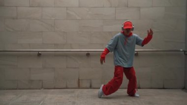 Yakışıklı koreograf gri arka planda sokak dansı yapıyor. Genç çekici erkek dansçı şık kıyafetler giyerken gösteri yapıyor. Hareketli bir adım. Uzayı kopyala Açık hava sporu 2024. Yumuşak bir şekilde..