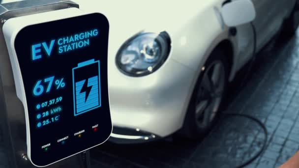 持智能手机的女商人通过智能电动车移动应用程序显示电池的状态接口 而生态友好型电动车则从停车场的充电站充电 仔细阅读 — 图库视频影像