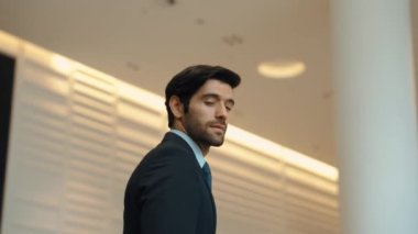 Profesyonel bir iş adamı kolları bağlıyken arkasını döner. Kafkasyalı mutlu yatırımcı, arka planı bulanık bir şekilde koridorda kollarını kavuştururken kameraya özgüvenle bakıyor. Portre. Sevinçli..