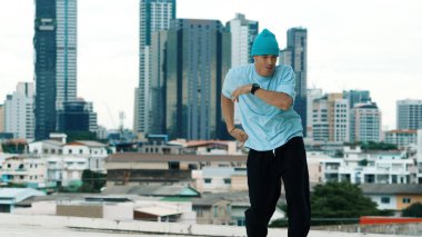 Beyaz tenli dansçı çocuk çatıda sokak dansı yapıyor şehir siteleriyle ya da şehirlerle. Genç adamın sokak dansı yaparken dondurucu poz vermesi. Açık hava sporu 2024. ÇalışmaComment.