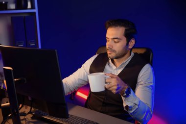 Gülümseyen zeki işadamı, elinde kahve fincanı olan satış ekibiyle buluşuyor ve geceleri Mor Neon Light Home Office 'deki bilgisayar ekranında ürün hedef pazarını araştırıyor. Tahmin et..