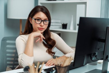 İş profili için poz vermek için gülümseyen güzel bir kadının portresi. Hem de masa başında çalışırken. Pozitif yeni nesil modern ofisin sabit teması. Varsayım.