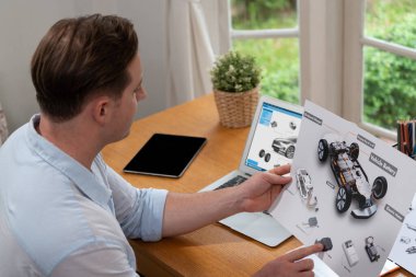 Araba tasarım mühendisi otomobil işi için otomobil prototipini ev ofisinde analiz ediyor. Otomotiv mühendisliği tasarımcısı dikkatle analiz ederek, dizüstü bilgisayarla araba tasarımında kusurlar ve iyileştirmeler buluyor.